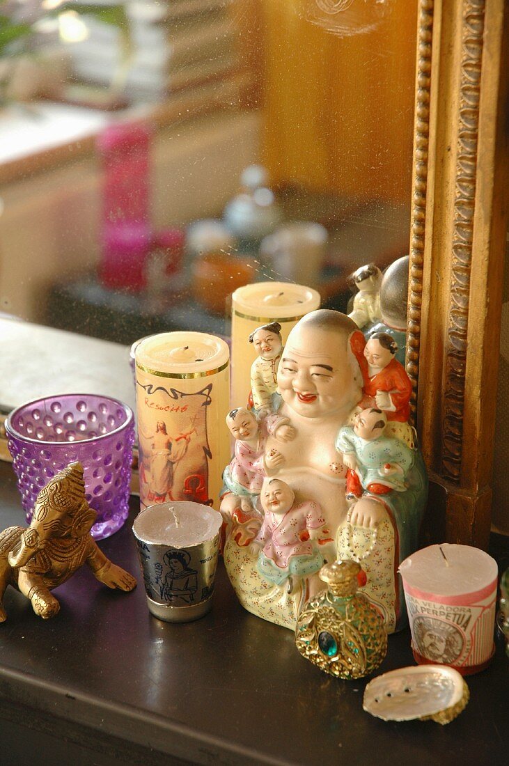 Votivkerzen um Keramik-Buddhafigur auf Ablage vor Goldrahmenspiegel