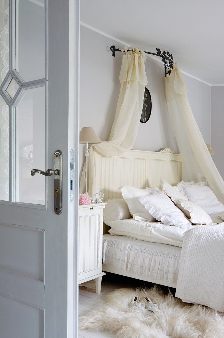 Doppelbett mit transparentem Baldachin, auf Boden weisses Tierfell in ländlichem Schlafzimmer