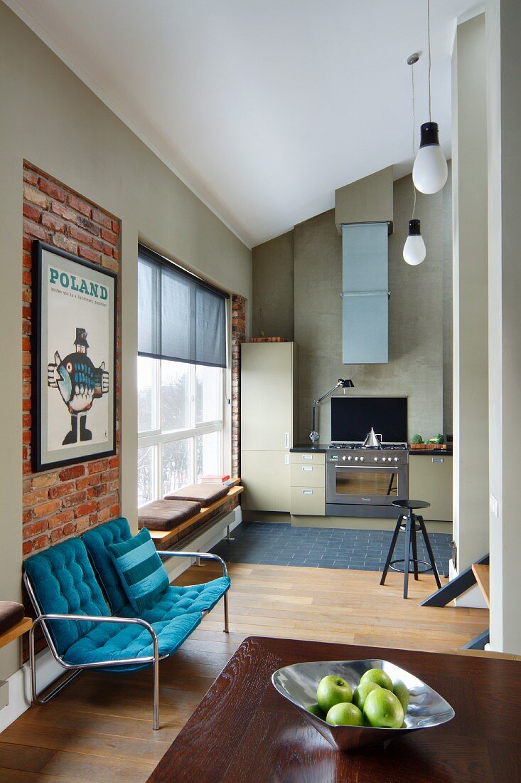Sitzbank mit blauen Polstern an Ziegelwand, im Hintergrund moderne Einbauküche in offenem Wohnraum