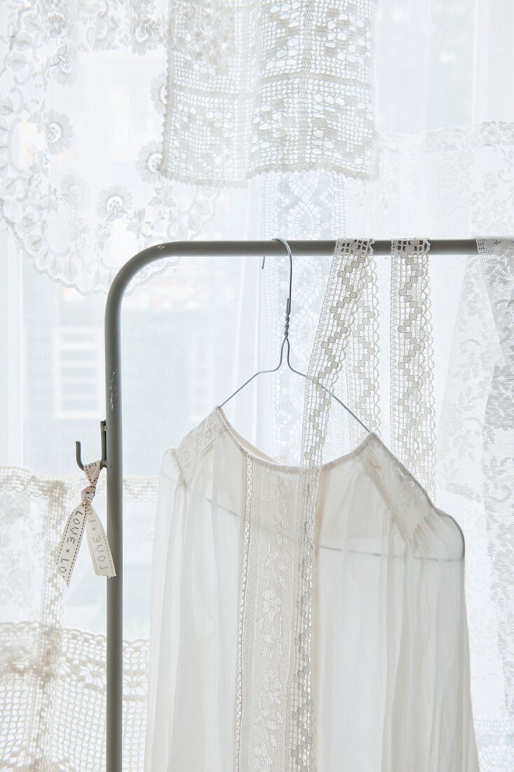 Lace top hanging from clothes rack in front of lace curtain