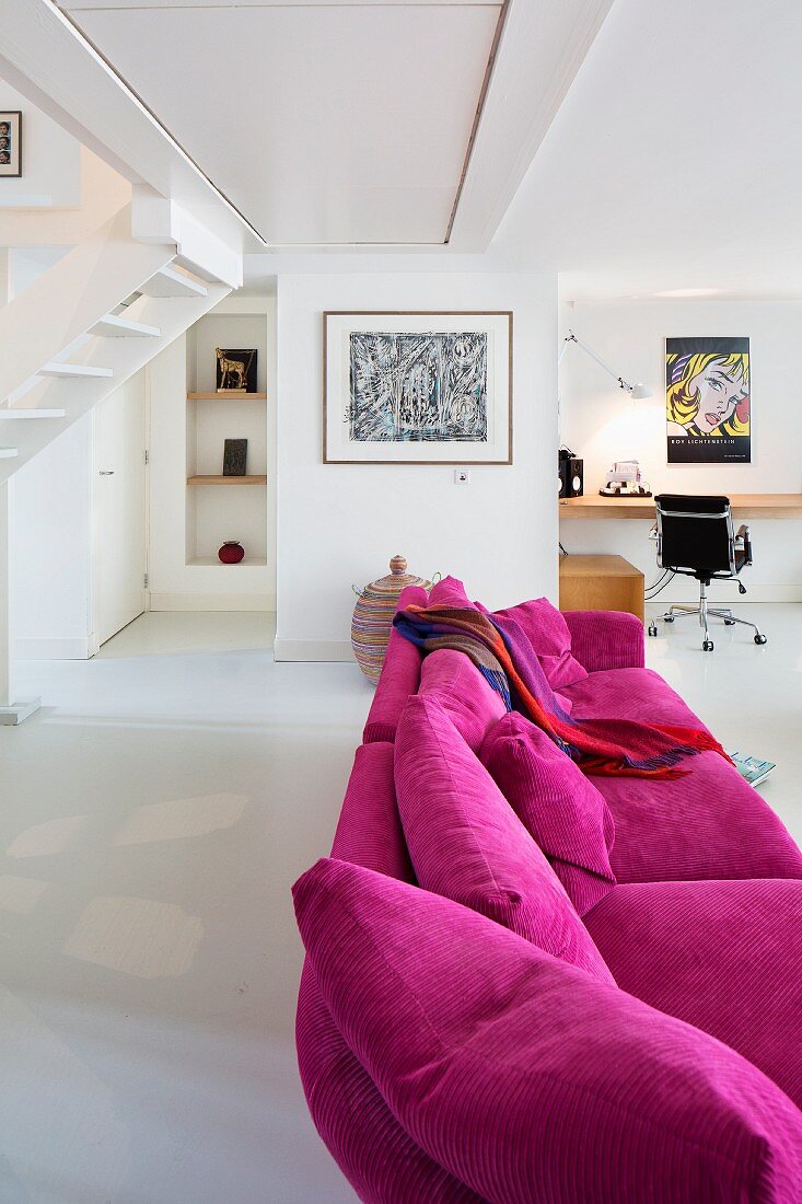 Magenta couch in modern, open-plan interior with desk and classic chair in background
