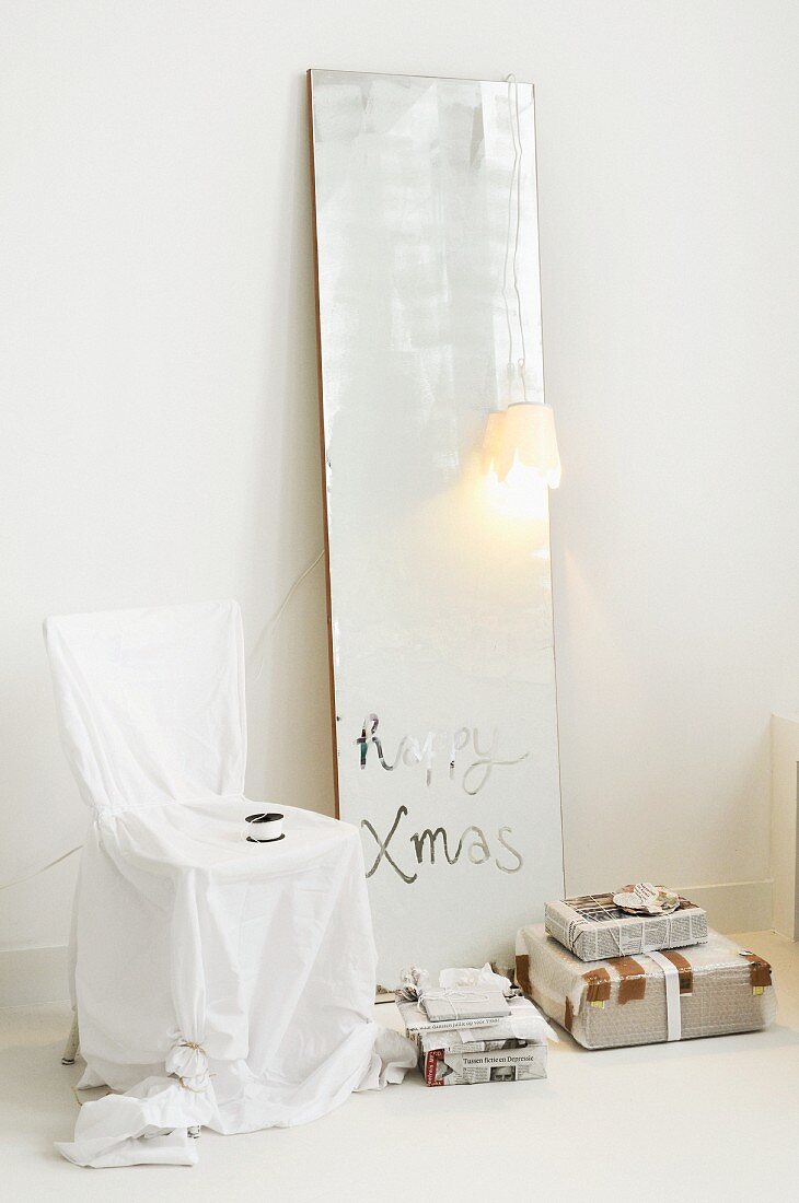 Ein blinder Spiegel mit Weihnachtsgruss, Stuhl mit Husse und Geschenke in Zeitungspapier