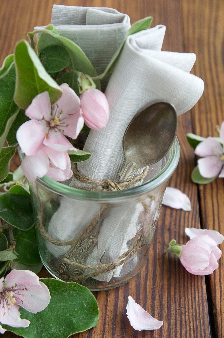 Silberlöffel mit Stoffserviette und Quittenblüten in Einmachglas