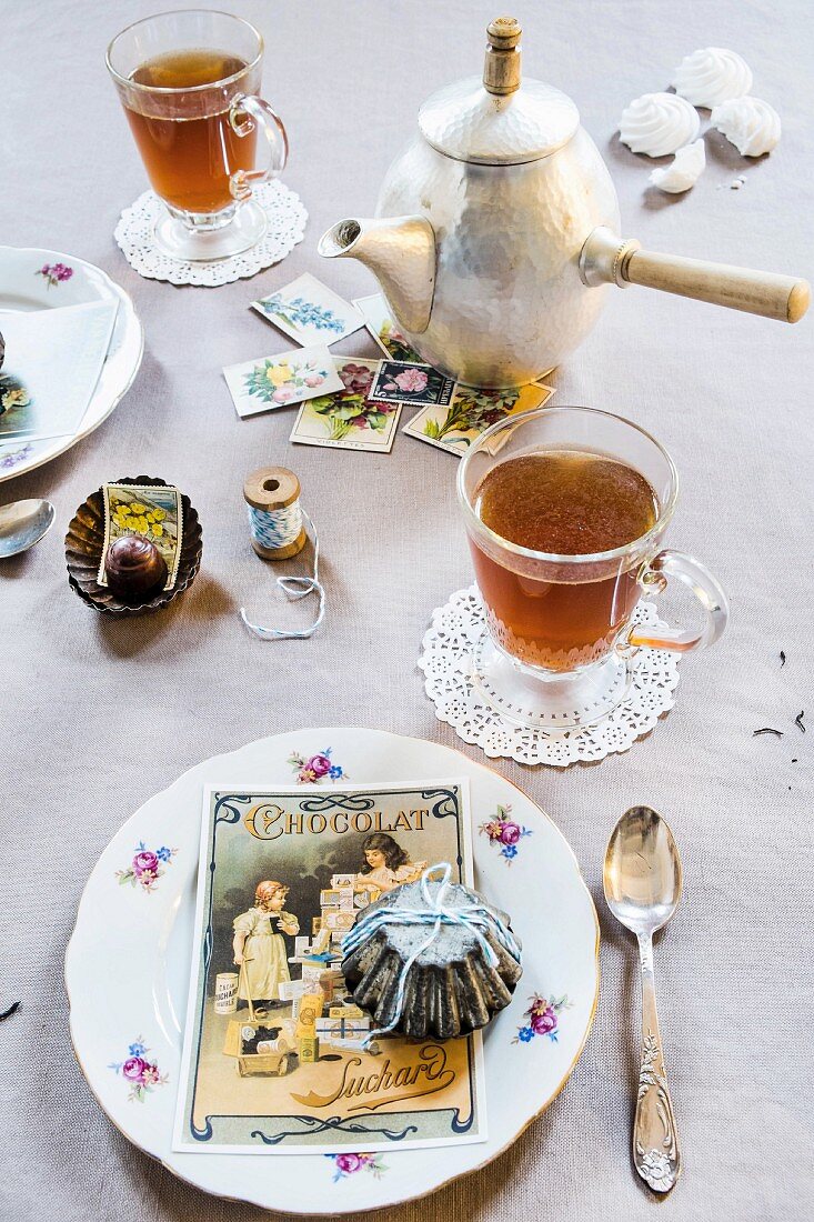 Vintage-style place setting on table with teacups, old cake tins and postcards