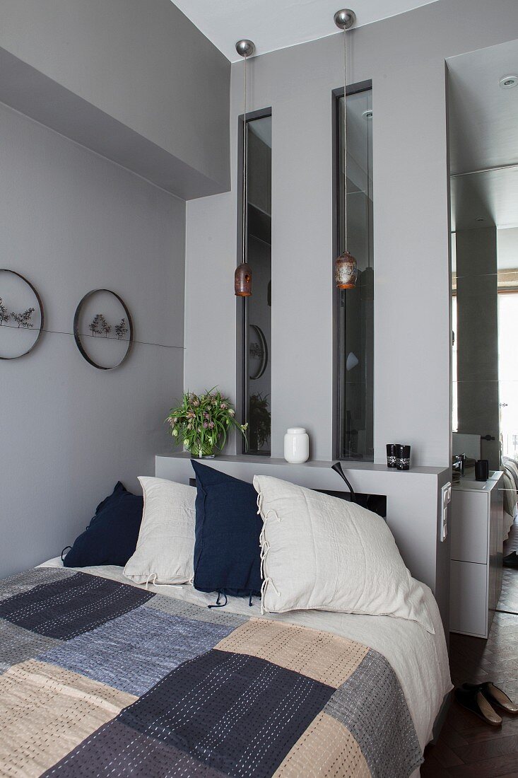 Bett mit Patchworkdecke vor einer grauen Wand mit Sims und Lichtfenstern