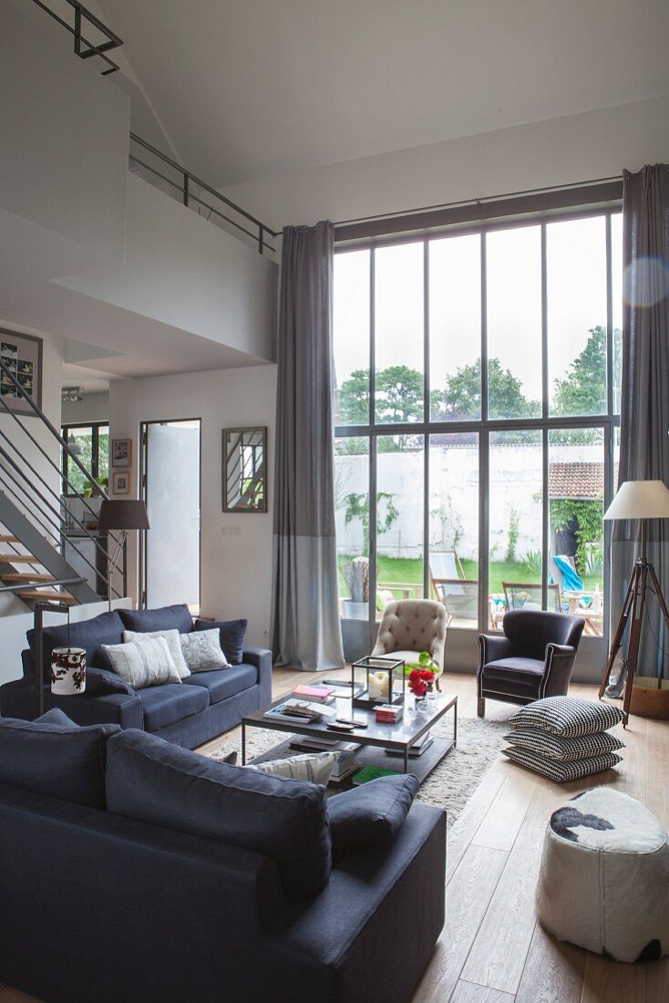 Hoher Lounge-Bereich in eleganten Grautönen mit Fensterfront zum Garten