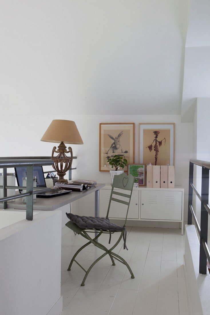Homeoffice auf weißer Galerieebene mit pastellgrünem Vintage-Gartenstuhl, antiker Tischlampe und Metallsidebord