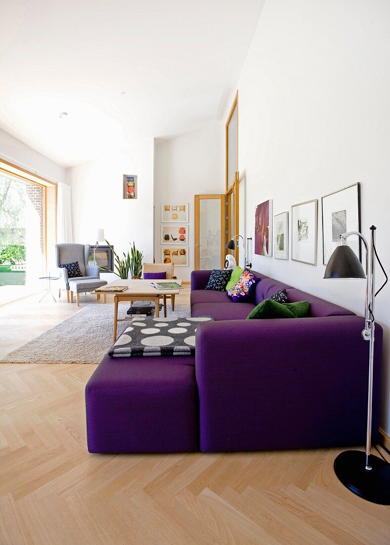 Lichtdurchflutetes Wohnzimmer mit lila Sofa auf Fischgrätboden und Retro Stehleuchte