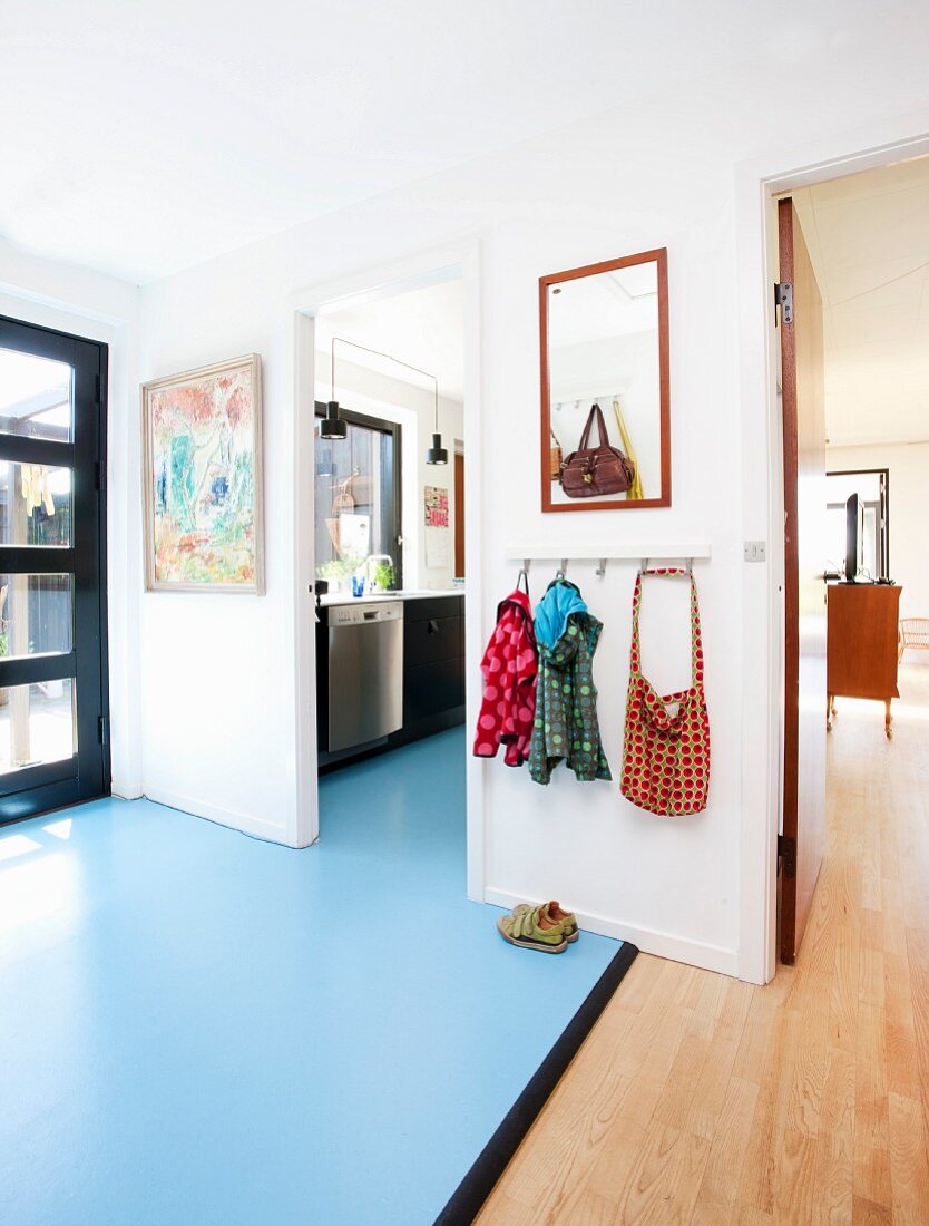 Vorraum mit unterschiedlichem Bodenbelag, hellblaues Linoleum und Parkett, an Wand Kindergarderobe neben Durchgang mit Blick in die Küche