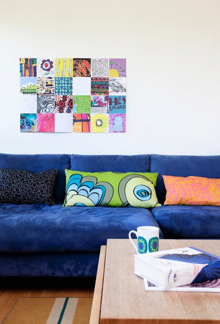Sofa with blue cover and row of patterned scatter cushions below modern artwork on wall