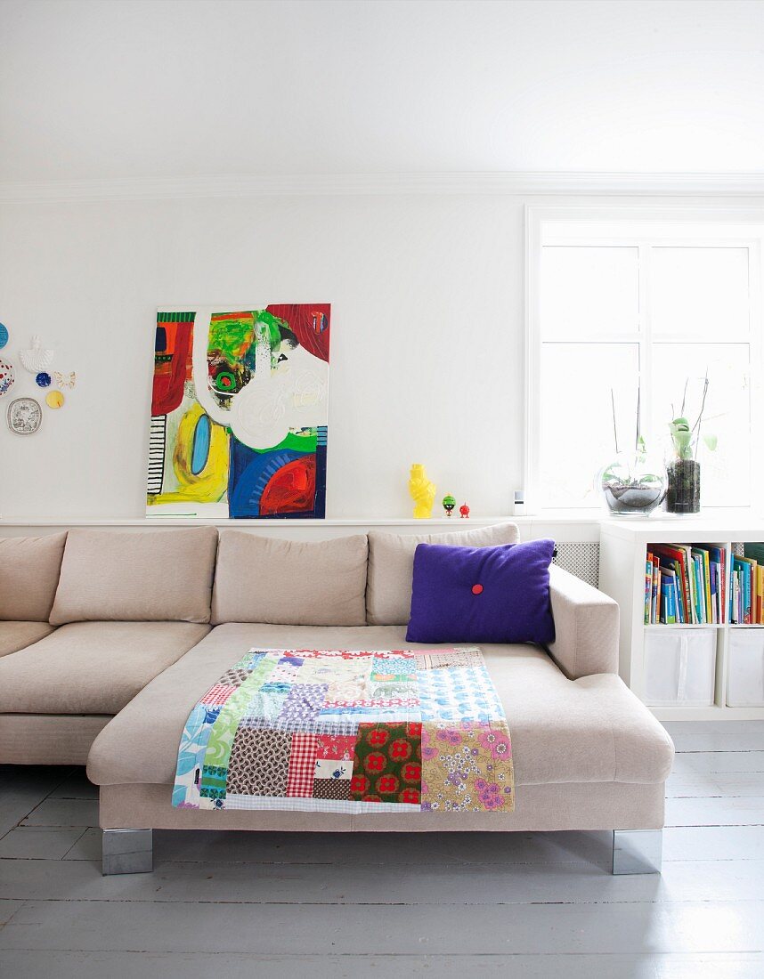 Patchwork blanket and purple scatter cushion on pale sofa combination and modern artwork on shelf leaning against wall