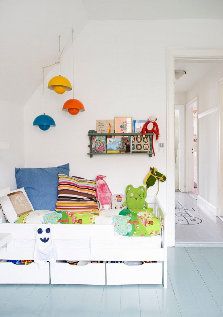 Weißes Kinderbett mit Bettschubladen und farbigen Pendelleuchten an Wandschräge