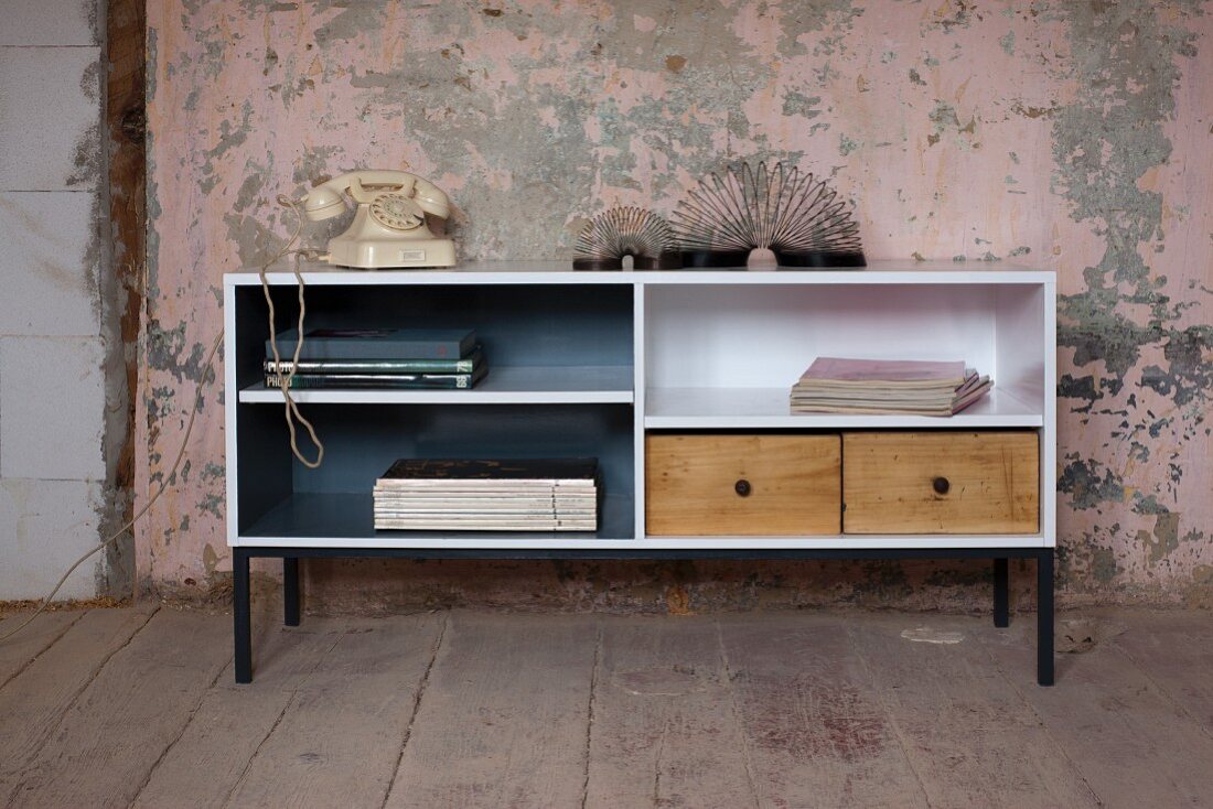 Upcycling - open-fronted sideboard painted white with wooden drawers against wall with peeling paint