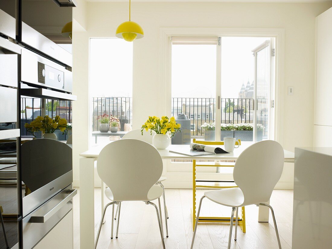 Essbereich mit weissen Schalenstühlen und gelbem Tripp Trapp vor Terrassentür