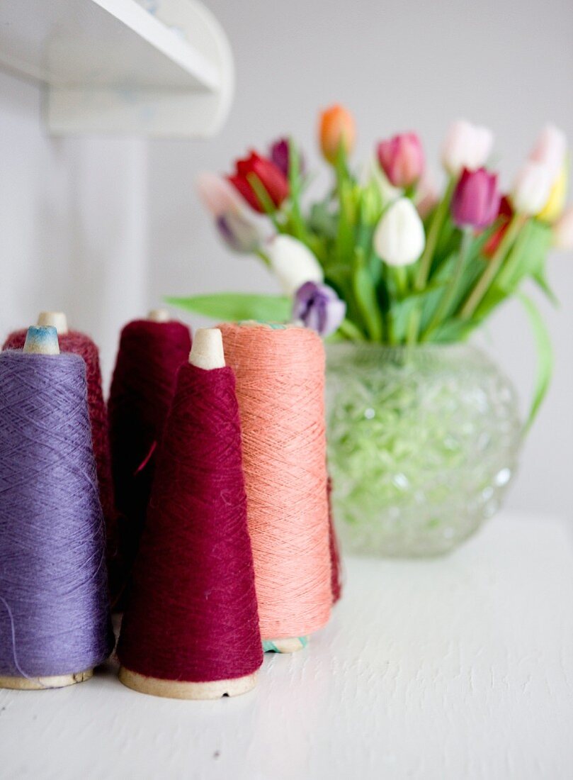 Colourful reels of thread with vase of tulips in blurred background