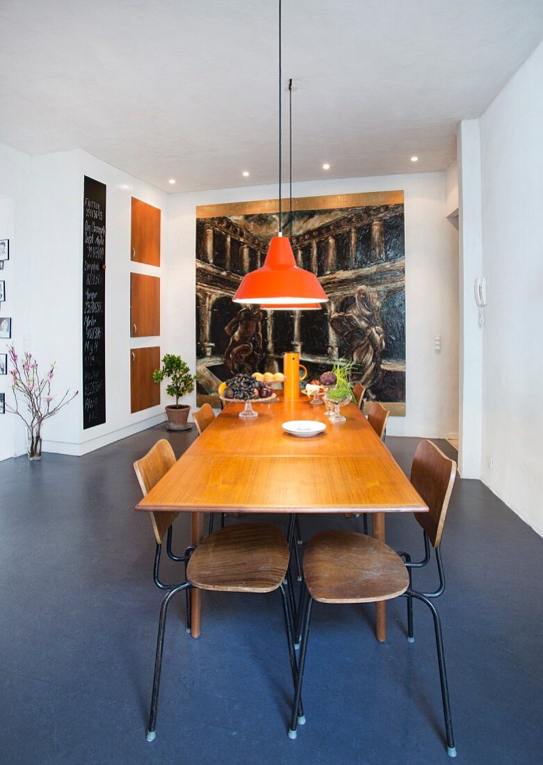 Extendible table, retro school chairs and orange pendant lamps in front of large painting in dining area