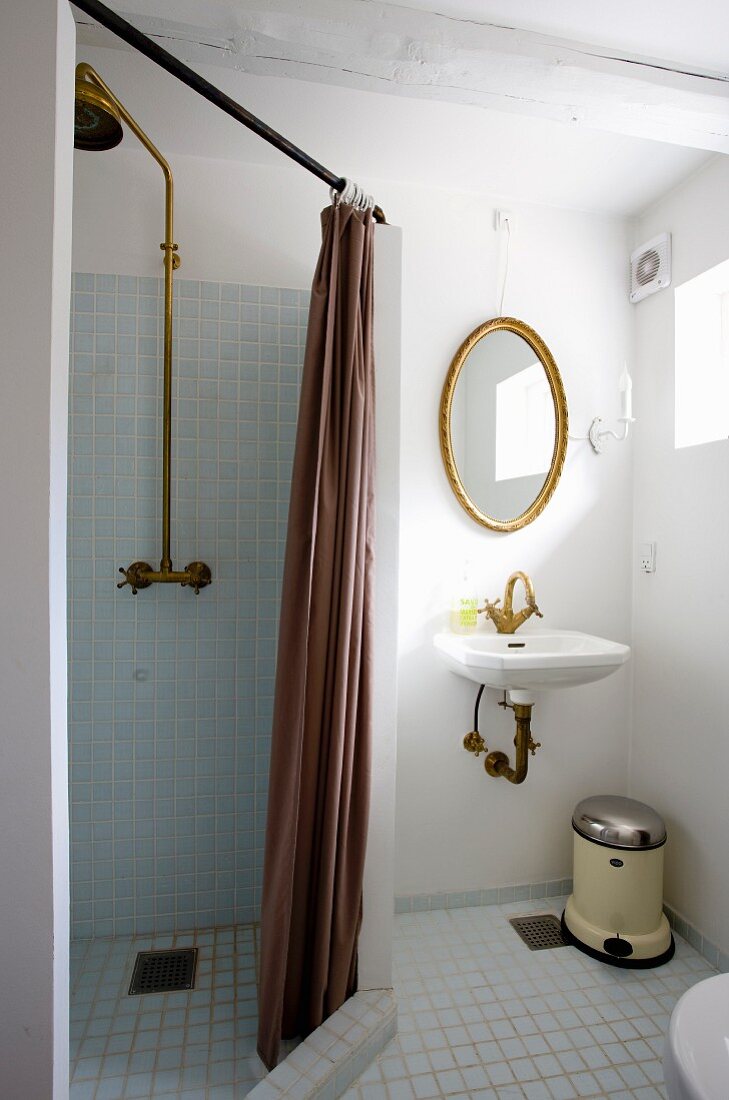 Abgetrennter Duschbereich mit braunem Vorhang, seitlich Waschbereich, ovaler Spiegel mit Goldrahmen an Wand