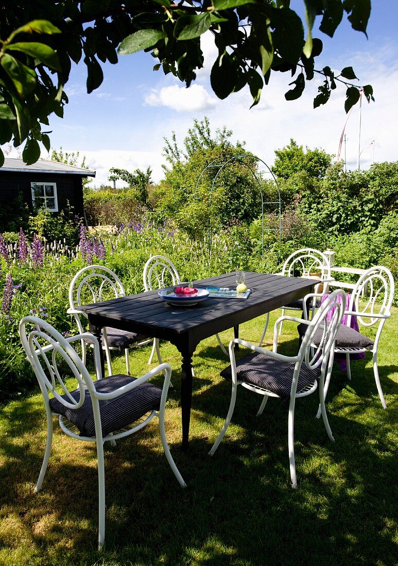 Holztisch mit weissen Stühlen aus gebogenem Metall in sommerlichem Garten