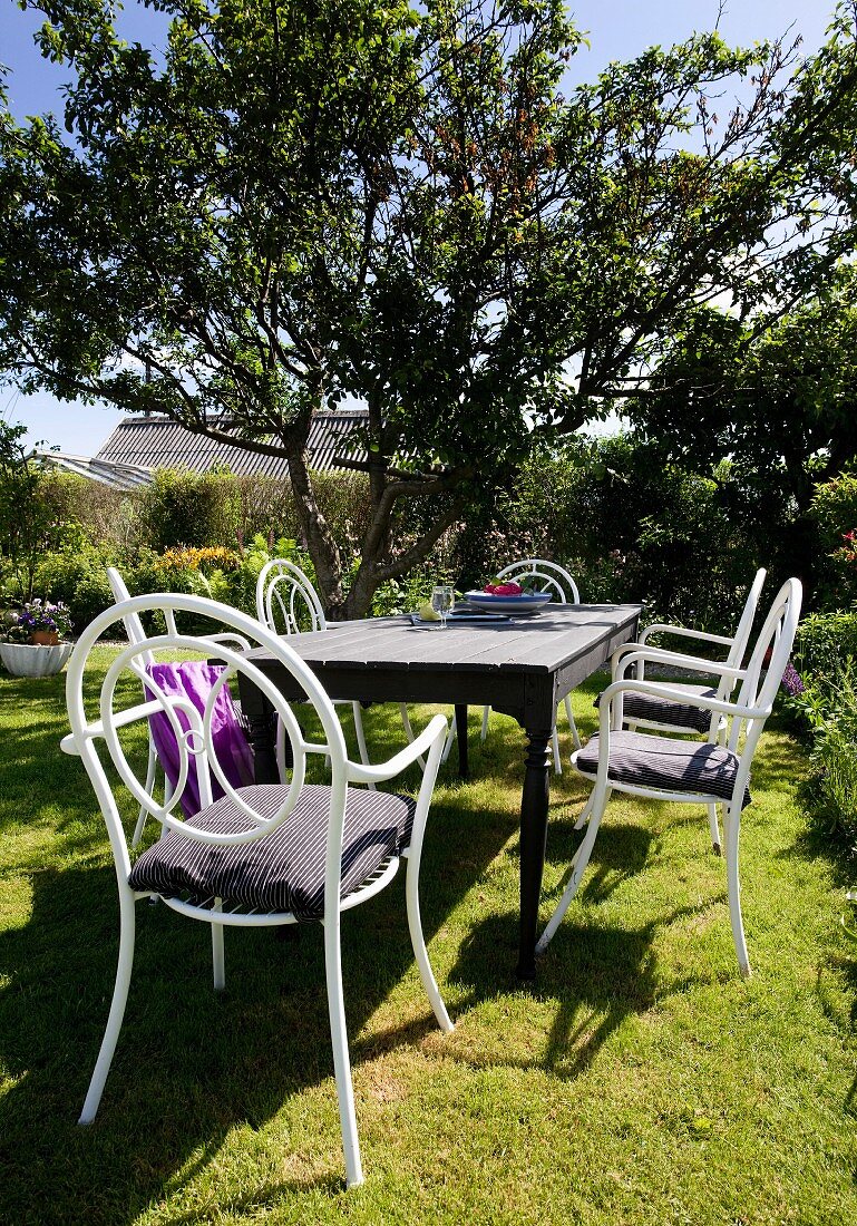Holztisch mit weissen Stühlen aus gebogenem Metall in sommerlichem Garten