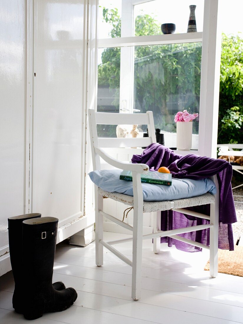 White wardrobe, wooden armchair with seat cushion and black boots next to French windows
