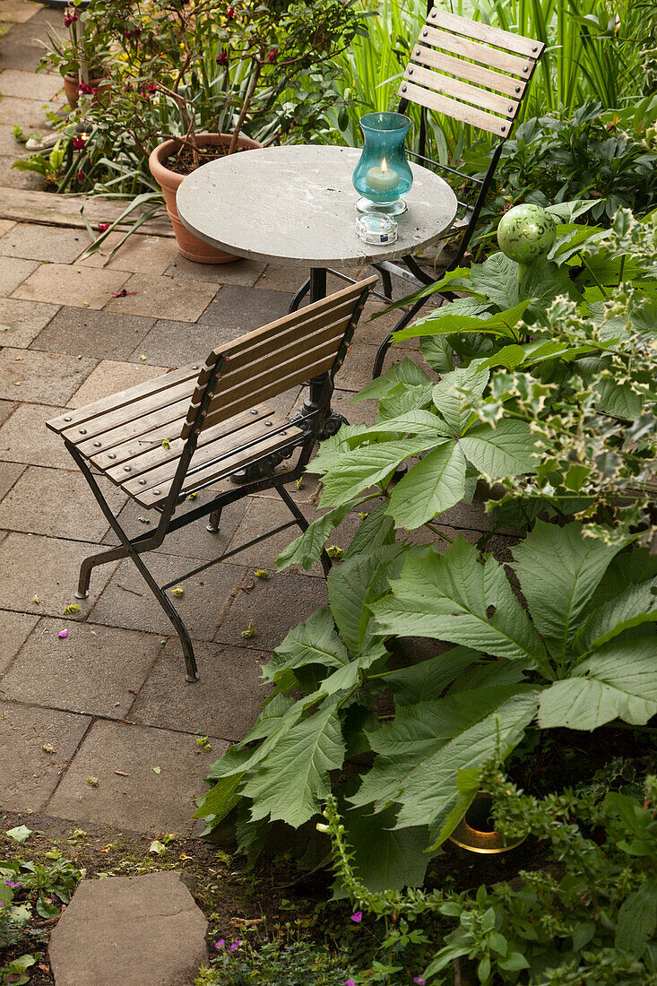 Gartenstühle und Tisch auf einer von Grünbeeten eingefassten Terrasse