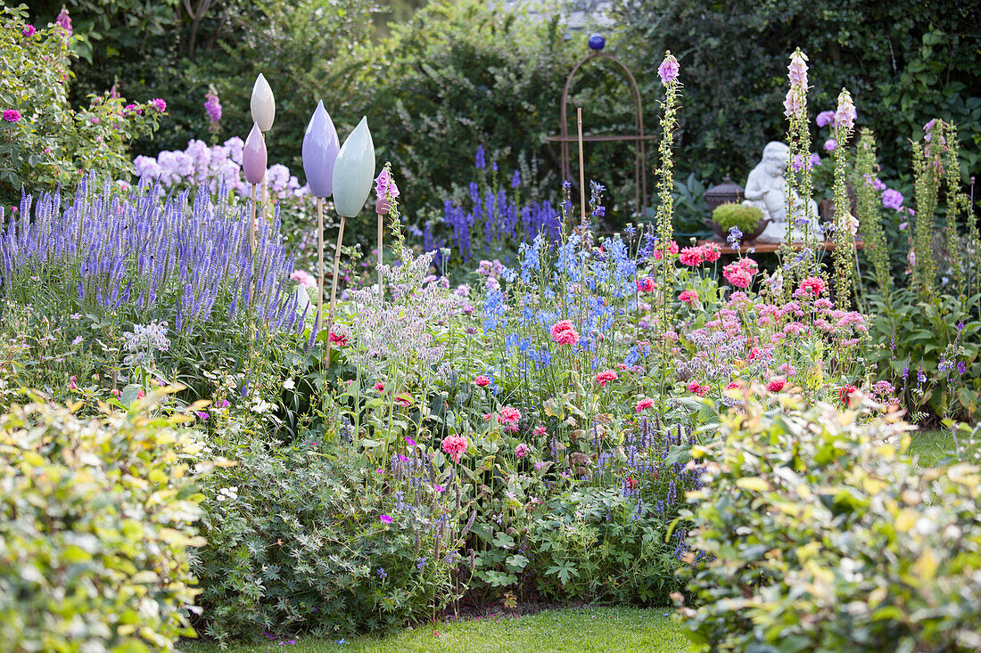 Blue veronica, foxgloves, corydalis and ornaments in flowering garden
