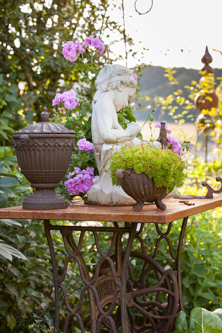 Vintage Nähmaschinentisch mit Pflanzengefässen und Steinfigur im Garten