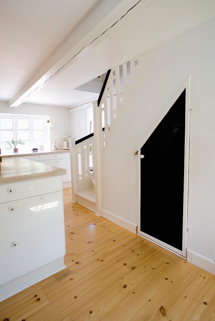 Offene Küche mit Theke, weiße Unterschränke, seitlich Treppenaufgang, darunter ausgebauter Stauraum mit schwarz lackierter Tür