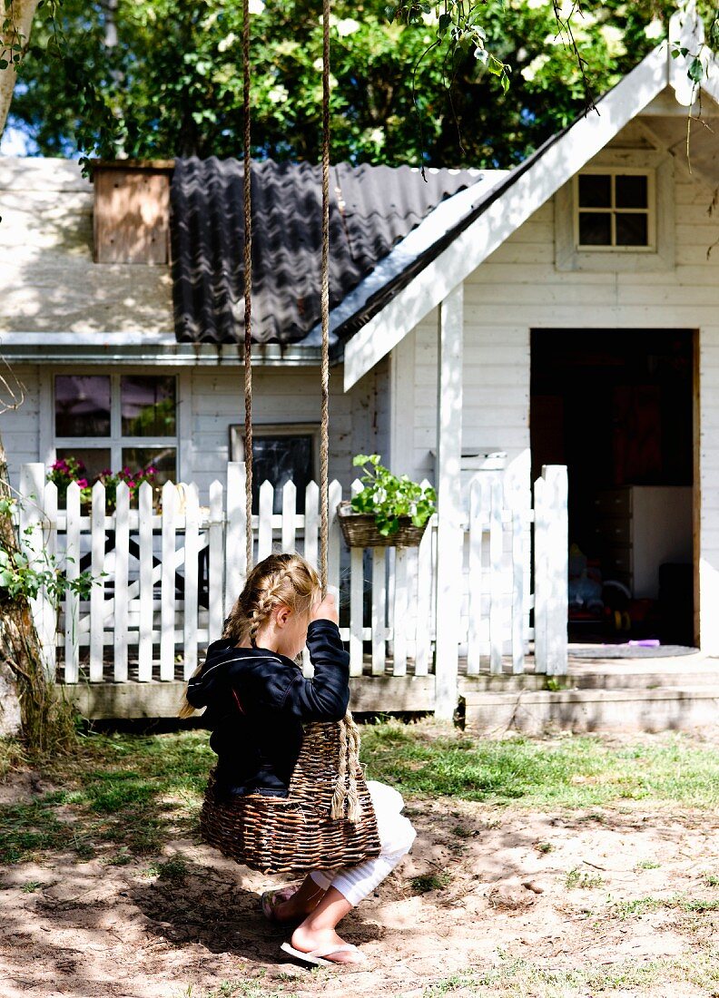 Little girl on wicker swing in front of white wooden house