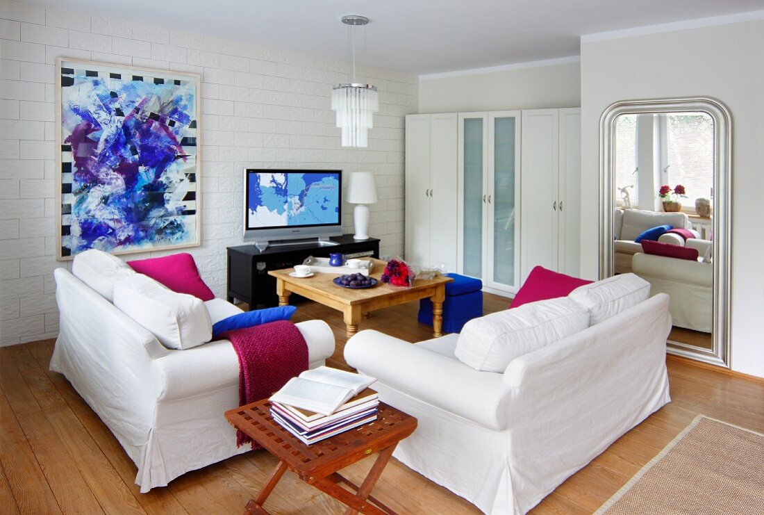 Weiß möbliertes Wohnzimmer mit starken Farbakzenten in Magenta und Königsblau