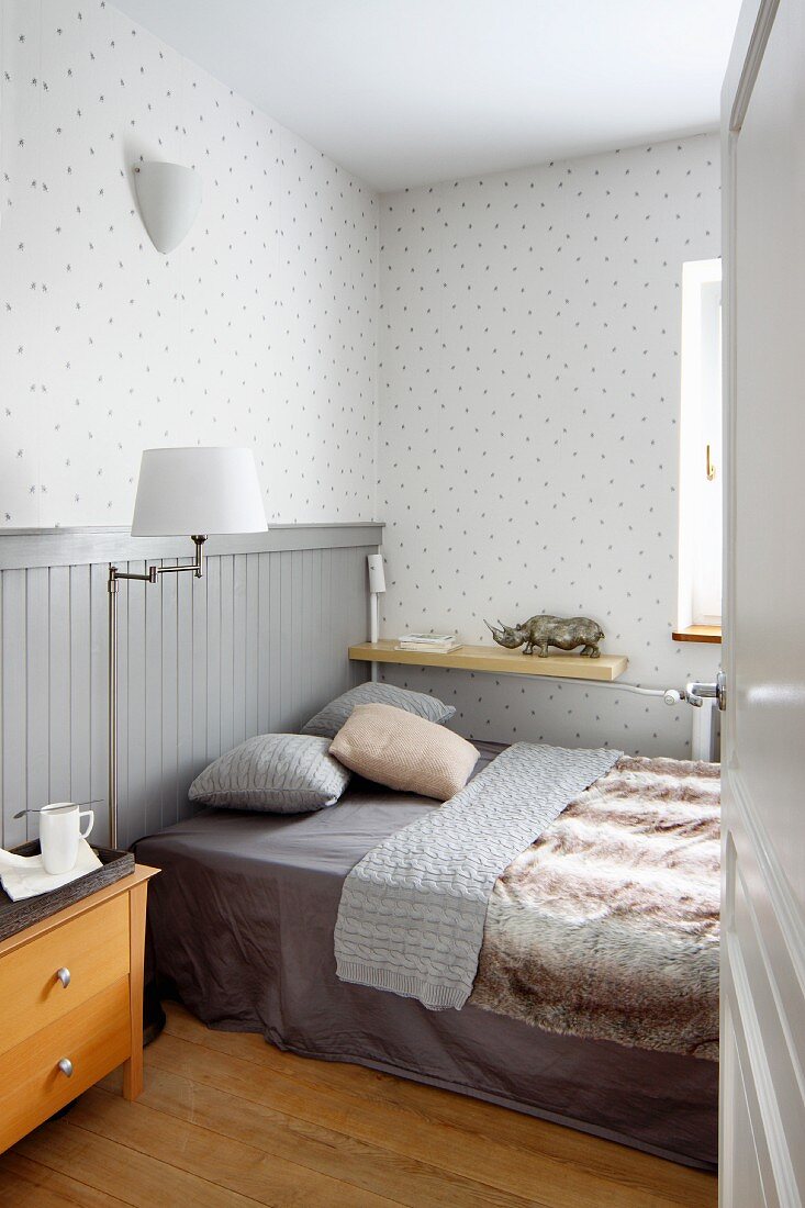 Schlafzimmer mit Doppelbett, halbhoher Holzvertäfelung und gepunkteter Tapete in Grautönen
