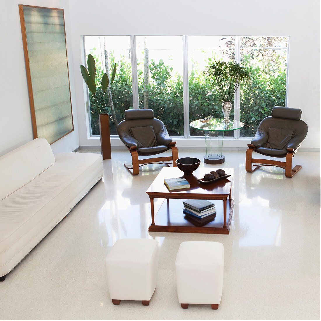 Modern living room with glossy, white floor, sofa, leather armchair, stools & coffee table in front of glass wall