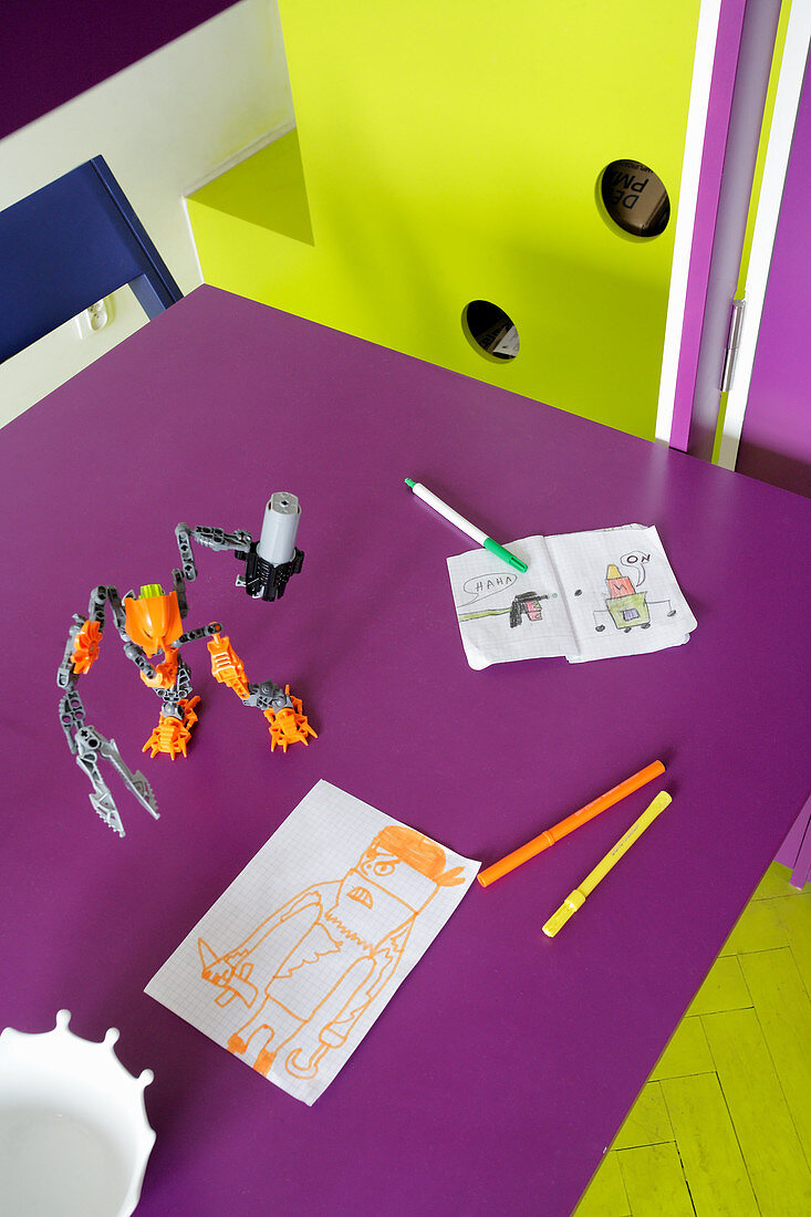 Child's drawings and toys on purple table with adjacent fitted furnishings and floor in complementary lime green