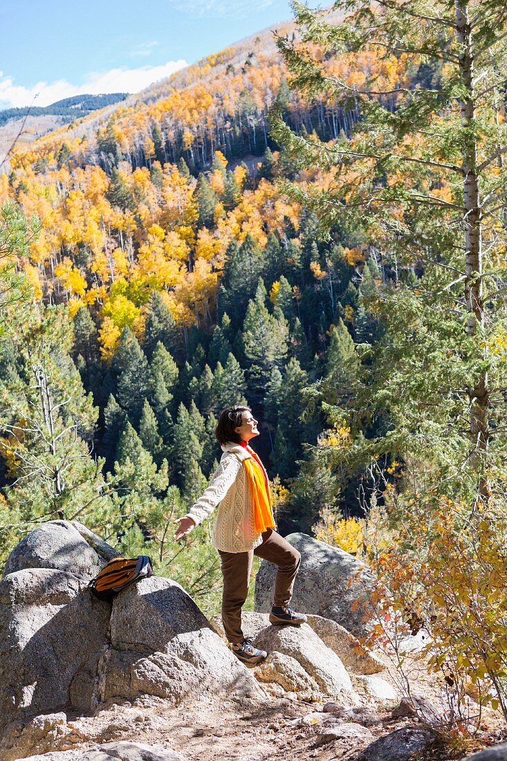 Woman wearing hiking gear standing with arm outstretched on rock ledge in autumnal mountain landscape