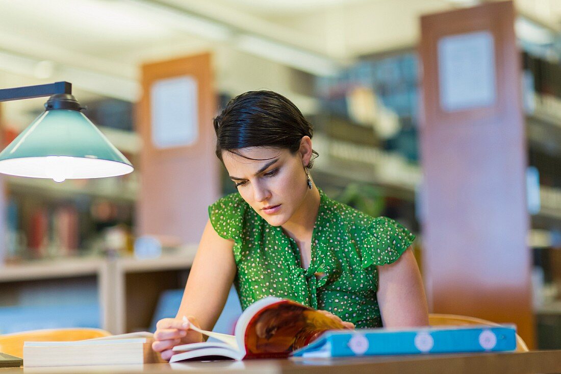Studentin sitzt lernend über Bücher gebeugt in Bibliothek