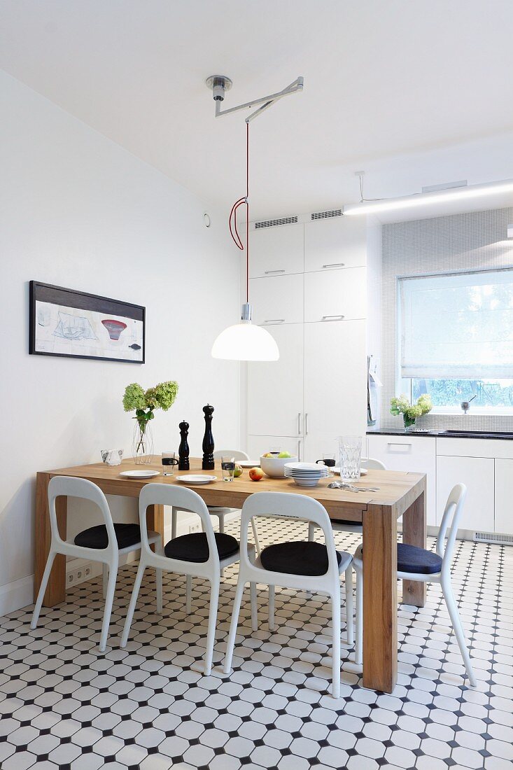 Massiver Holztisch und weiße Retro Stühle in moderner Küche mit weissgrauem Fliesenmosaik am Boden