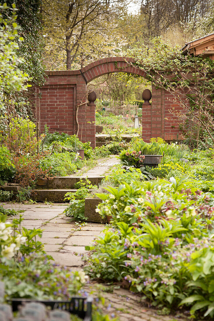 Angelegte Beete in idyllischem Garten, im Hintergrund Ziegelmauer mit integriertem Torbogen