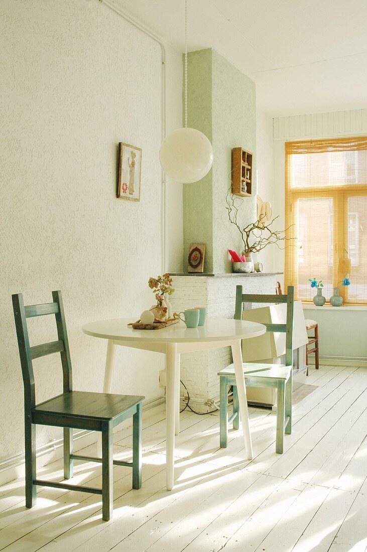 Dining area with round table and green, wooden chairs in bright interior with white wooden floor