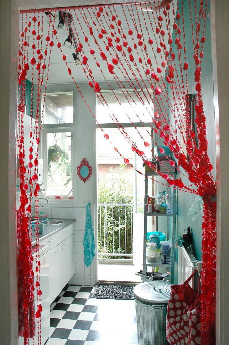Blick durch drapierten, roten Perlenvorhang in winzige Küche mit Balkon