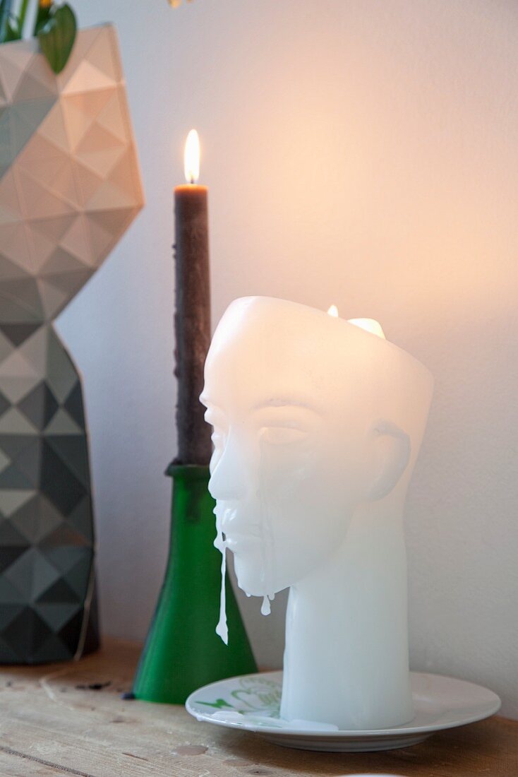 Head-shaped wax candle next to lit candle in green candlestick
