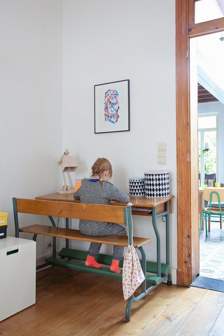 Kleines Mädchen an Tisch-Bankkombination vor Wand, neben teilweise sichtbaren Durchgang