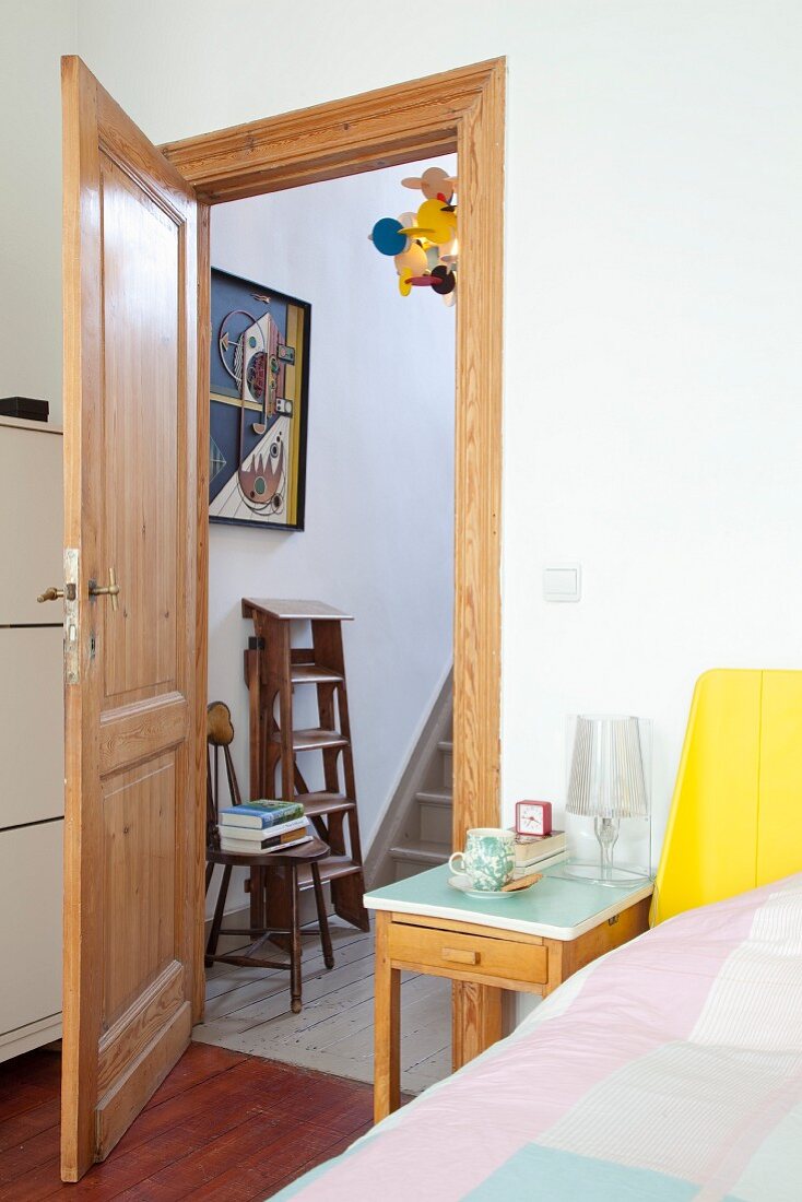 Ausschnitt eines Schlafzimmers, Nachttisch neben Bett und offener Zimmertür aus Holz mit Blick ins Treppenhaus