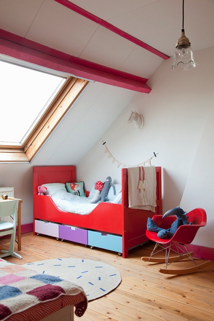 Classic rocking chair with red shell seat next to red sleigh bed in child's attic bedroom