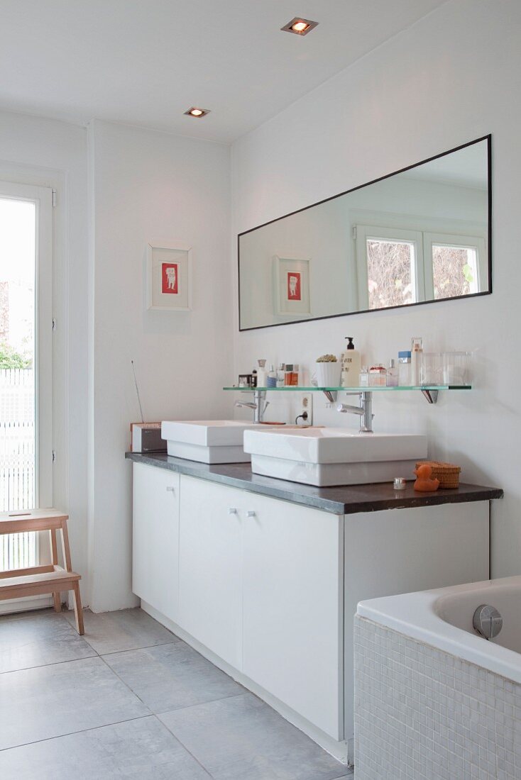 Modern washstand with white base units and twin countertop basins below wide mirror on wall