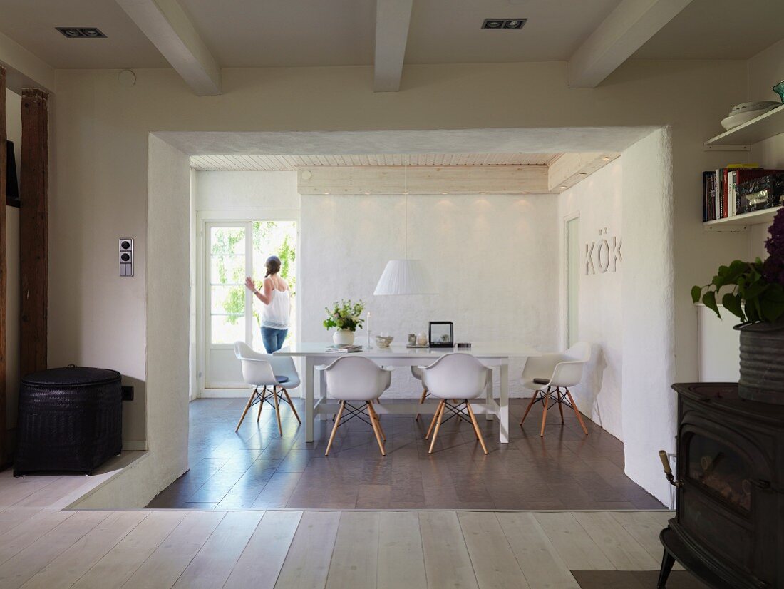 Abgesenkter Essbereich mit Fliesenboden und Designerstühlen vor geöffneter Terrassentür mit Frau in renoviertem Landhaus