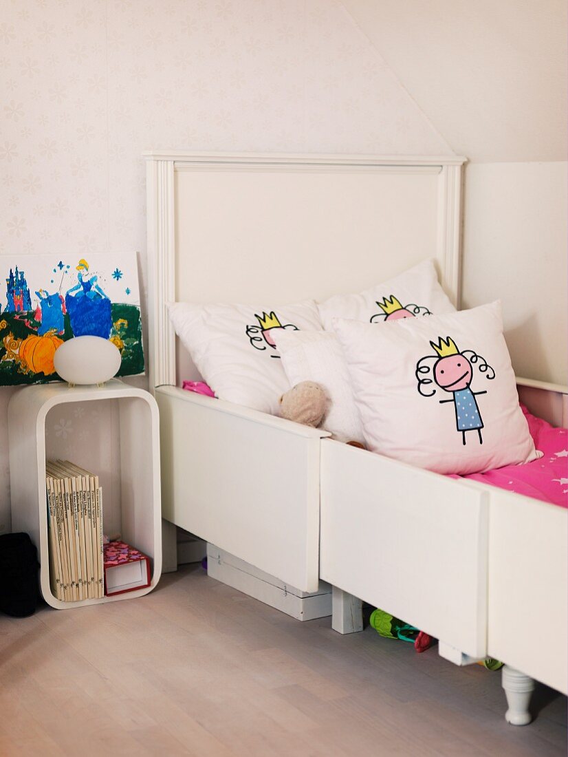 Mädchenzimmer mit weißem ausziehbarem Bett und Dekokissen, Nachttisch mit Retroflair