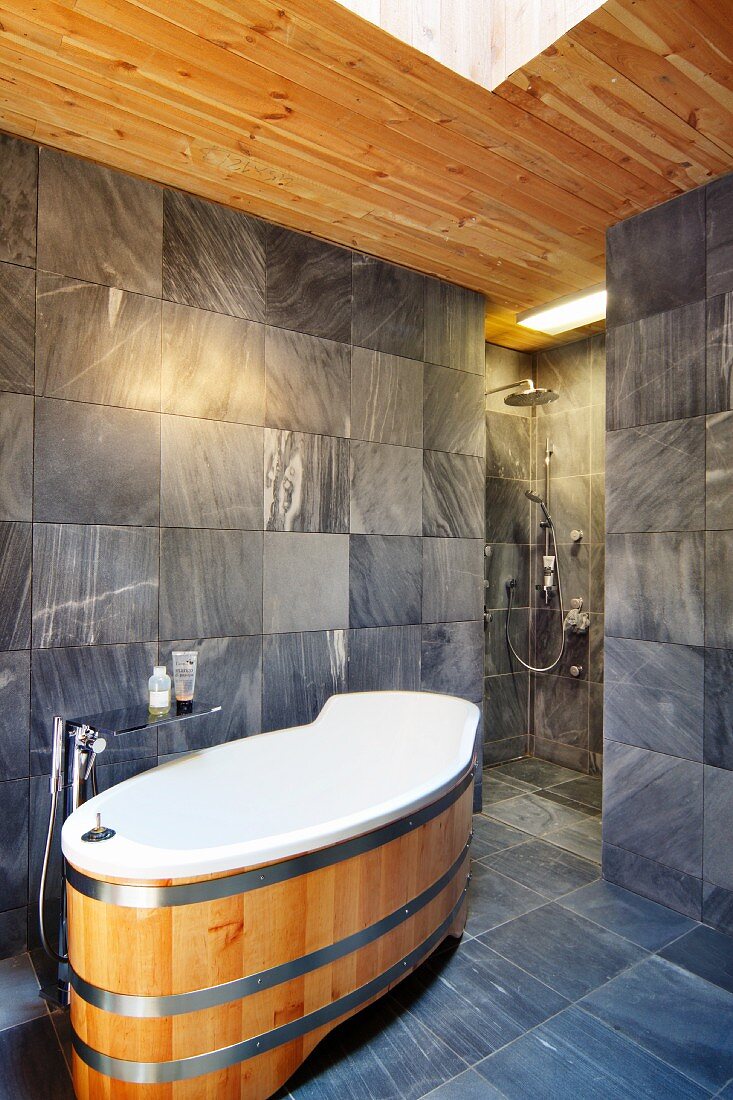 Designerbad mit Wanne im modernen Fass-Design und grauen Fliesen, offene Dusche im Hintergrund