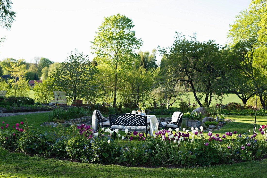 Idyllischer Sitzplatz im Garten, blühende Tulpen in angelegtem Beet