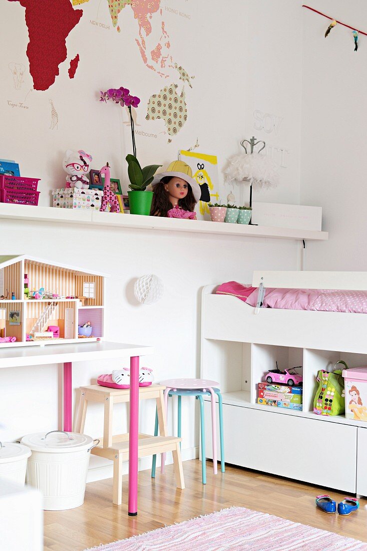 Weisses Hochbett mit Regalunterbau, Wandboard mit Spielsachen und Puppenhaus auf Tisch im Mädchenzimmer