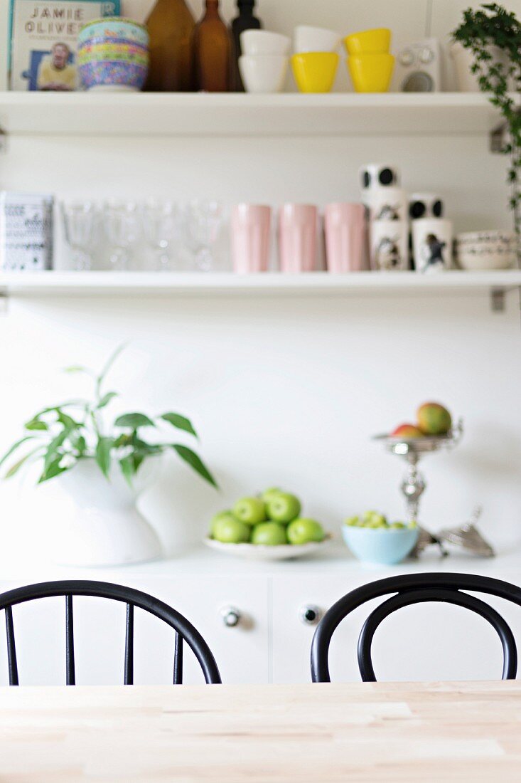 Dining table, black chairs, fruit bowl on sideboard and wall-mounted shelves